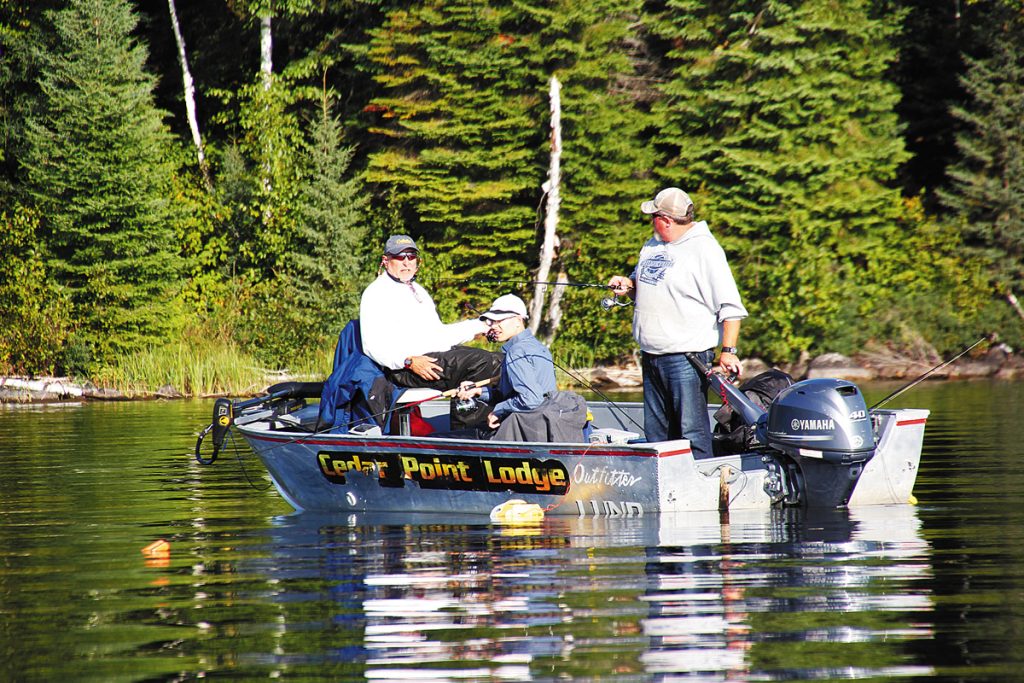 Three fishermen on a motorboat labeled Cedar Point Lodge outfitter, fishing on the calm waters of Eagle Mountain Lake near Azle, Texas, with a dense evergreen forest in the background.