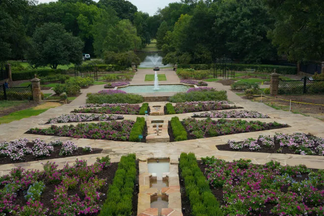 A high-angle view of the formal stone pathways and geometric flower beds at the Dallas Arboretum and Botanical Garden, featuring tiered fountains and pink and purple blooms—a perfect day trip for those RV camping near Fort Worth.