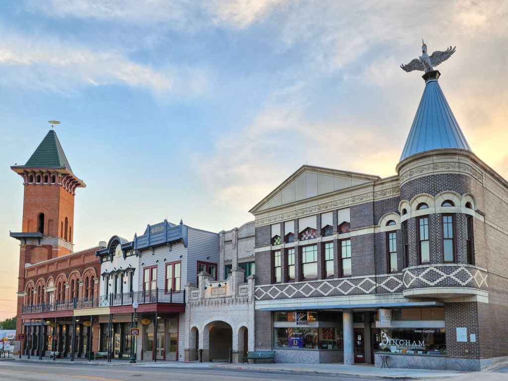 The charming historic Main Street of Grapevine, Texas, featuring beautifully restored brick buildings, a prominent clock tower, and a unique turret topped with a silver eagle statue against a soft sunset sky—a perfect day trip for those RV camping near Fort Worth.