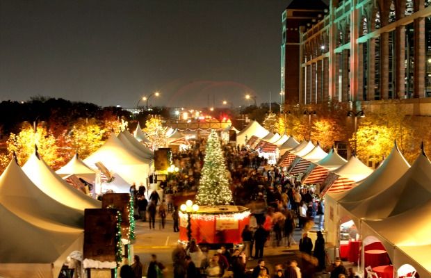 A vibrant high-angle nighttime view of the Texas Christkindl Market in Arlington, featuring rows of white peaked tents, a large lit Christmas tree, and crowds of people enjoying the festive atmosphere—a top holiday event near Azle and Fort Worth.