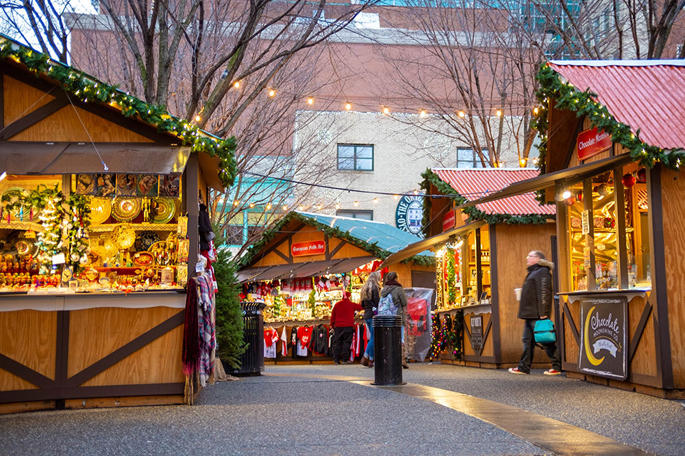 A charming outdoor Christmas market featuring wooden vendor stalls decorated with evergreen garlands and warm string lights, with shoppers browsing unique gifts—a must-see for those looking for holiday things to do in Azle.